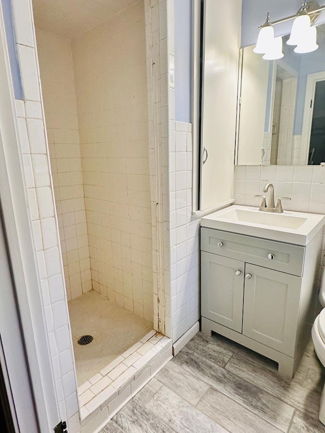 bathroom featuring toilet, a tile shower, tile walls, and vanity