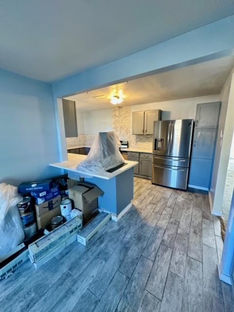 kitchen featuring kitchen peninsula, stainless steel fridge, a kitchen breakfast bar, hardwood / wood-style floors, and gray cabinets