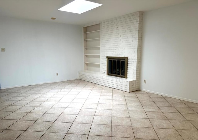 unfurnished living room featuring light tile patterned floors, built in shelves, a skylight, baseboards, and a brick fireplace