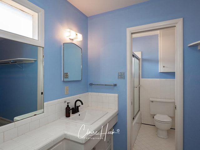 bathroom with toilet, a wainscoted wall, tile patterned floors, vanity, and tile walls