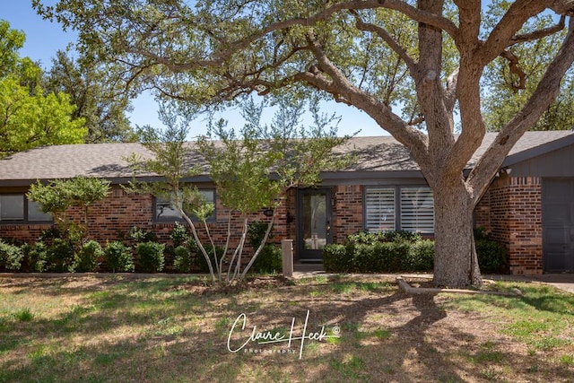 ranch-style home featuring roof with shingles and brick siding