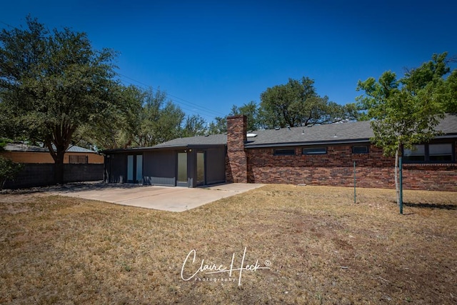 rear view of house featuring a patio, brick siding, fence, a yard, and a chimney