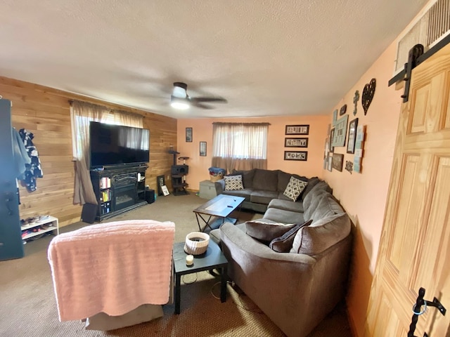 living room featuring carpet flooring, wood walls, ceiling fan, and a textured ceiling