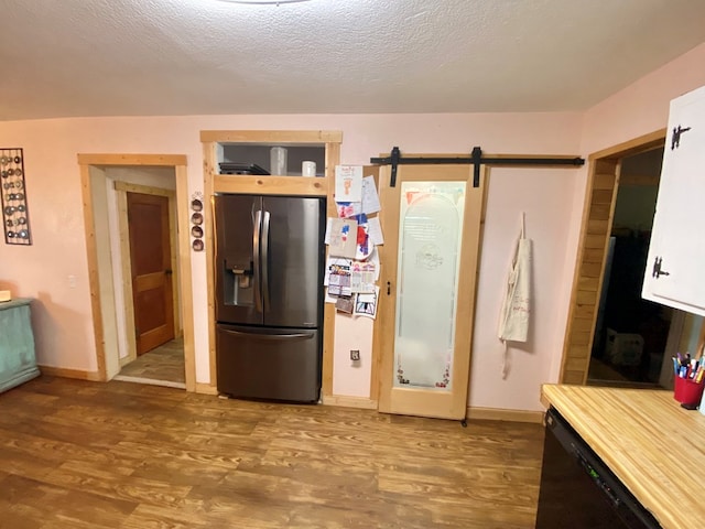 kitchen featuring dishwasher, hardwood / wood-style flooring, stainless steel fridge, a barn door, and a textured ceiling