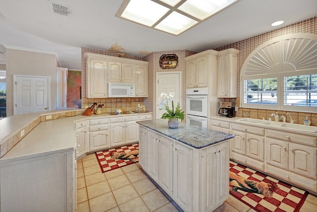 kitchen featuring a kitchen island, sink, decorative backsplash, kitchen peninsula, and white appliances