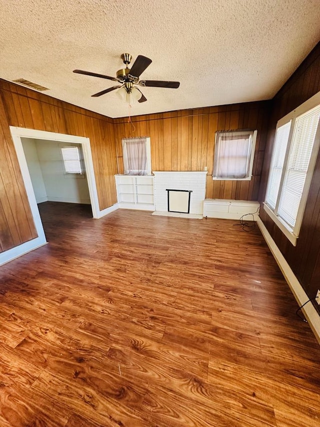 unfurnished living room featuring ceiling fan, wood walls, a textured ceiling, and hardwood / wood-style floors