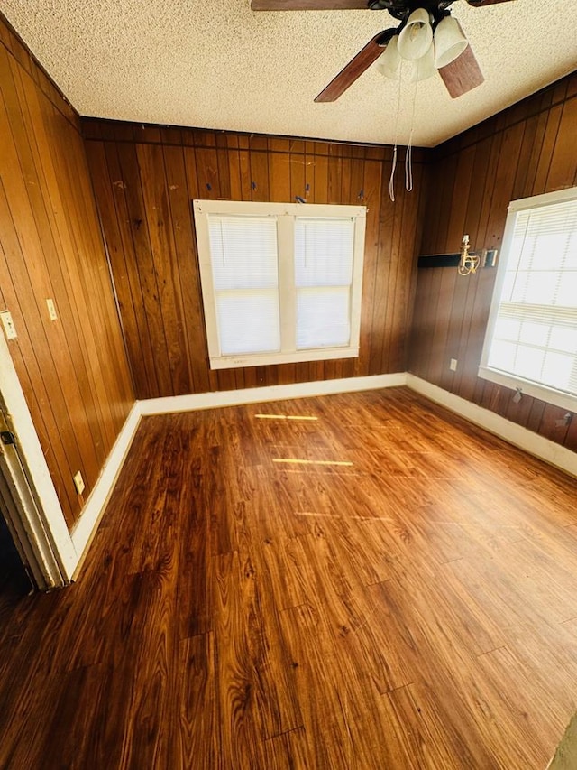 unfurnished room with a textured ceiling, ceiling fan, wood-type flooring, and wooden walls