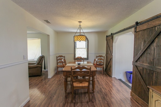 dining space featuring a textured ceiling, a barn door, and dark wood-type flooring