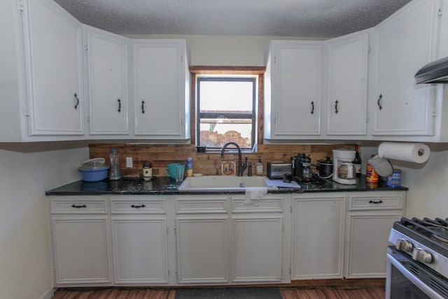 kitchen with a textured ceiling, stainless steel range oven, white cabinets, dark stone countertops, and sink