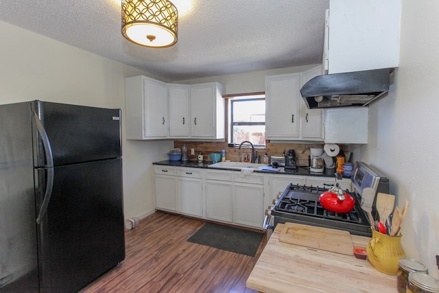 kitchen with black refrigerator, stainless steel gas range oven, sink, white cabinetry, and tasteful backsplash