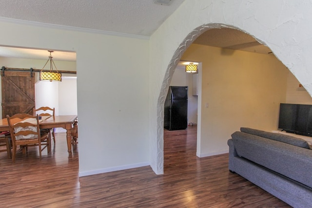 interior space with ornamental molding, a textured ceiling, a barn door, and dark hardwood / wood-style flooring