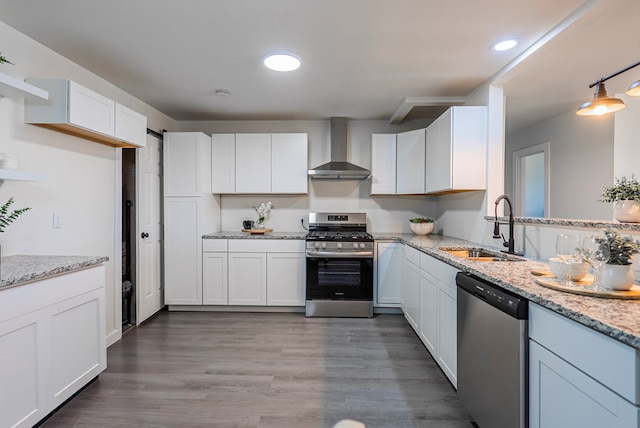4604 Versailles Dr, Midland, TX 79703 - kitchen featuring appliances with stainless steel finishes, wall chimney exhaust hood, white cabinetry, light stone counters, and wood finished floors