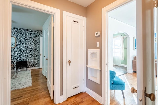 hallway with light wood-type flooring, arched walkways, and baseboards