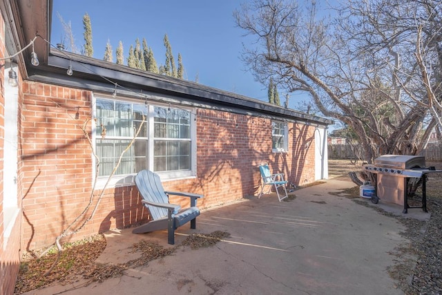 view of side of property featuring a patio area, brick siding, and fence