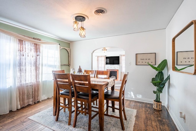 dining area featuring arched walkways, visible vents, a fireplace, and hardwood / wood-style flooring