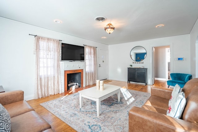 living room with baseboards, a fireplace with flush hearth, visible vents, and wood finished floors