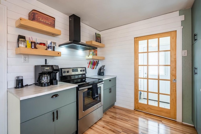 kitchen with light wood-style flooring, stainless steel electric stove, light countertops, wall chimney range hood, and open shelves