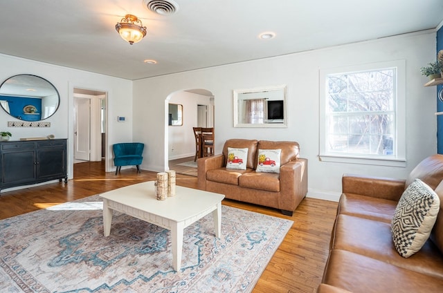 living room featuring light wood-type flooring, visible vents, arched walkways, and baseboards