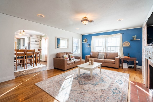 living room featuring a fireplace with flush hearth, arched walkways, baseboards, and wood finished floors