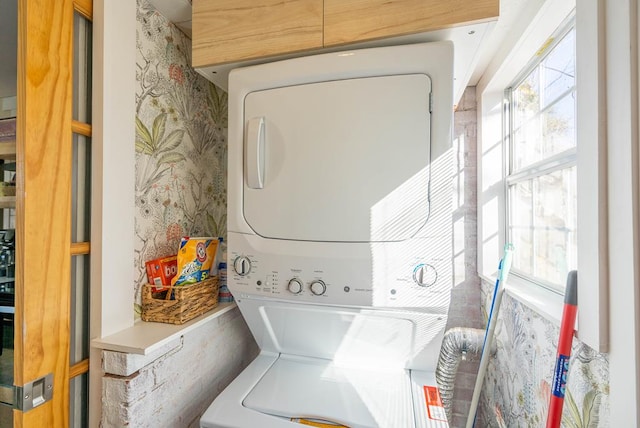 washroom with laundry area, stacked washer / dryer, and wallpapered walls