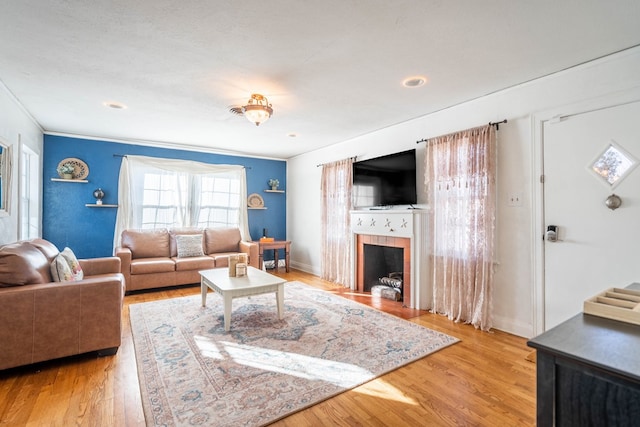 living area with a tiled fireplace, baseboards, wood finished floors, and ornamental molding