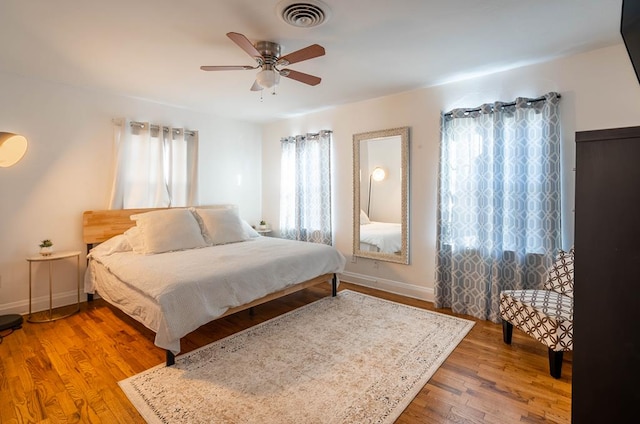 bedroom featuring visible vents, ceiling fan, baseboards, and wood finished floors