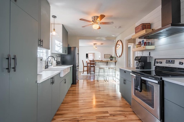 kitchen with light wood finished floors, stainless steel appliances, gray cabinetry, wall chimney range hood, and a sink