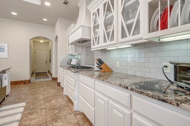 kitchen with arched walkways, baseboards, backsplash, light stone counters, and white cabinets