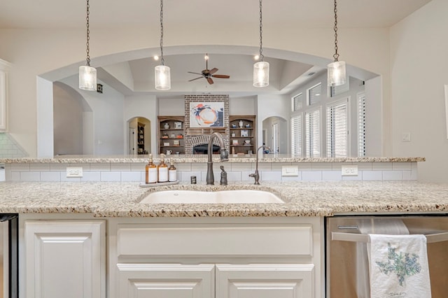 kitchen featuring dishwasher, a sink, a raised ceiling, ceiling fan, and arched walkways