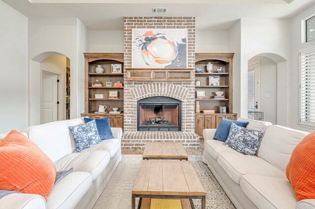 living room with arched walkways, a brick fireplace, built in features, and plenty of natural light