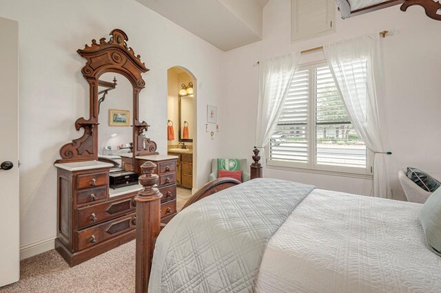 bedroom featuring arched walkways, light carpet, ensuite bathroom, and baseboards