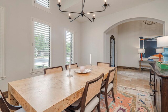 dining room with arched walkways, stone tile floors, plenty of natural light, and a chandelier