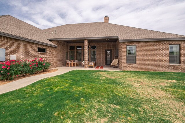 back of property with brick siding, a chimney, a yard, a patio area, and roof with shingles