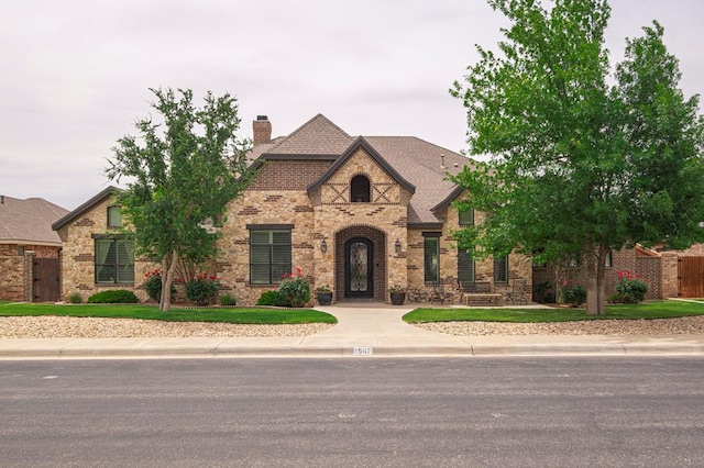 view of front facade featuring a chimney, fence, stone siding, and brick siding