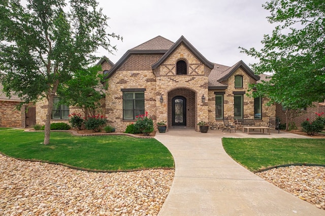 view of front of home featuring a front lawn, stone siding, brick siding, and a shingled roof