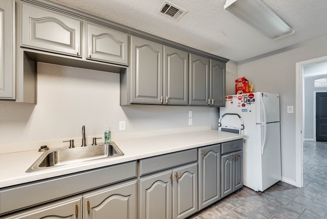 5709 E County Rd 97, Midland, TX 79706 - kitchen with light countertops, a sink, freestanding refrigerator, gray cabinetry, and visible vents
