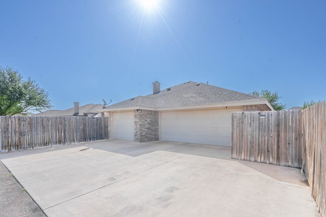 view of side of home with a garage, driveway, brick siding, roof with shingles, and fence