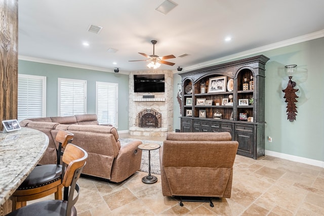 living area featuring a stone fireplace, baseboards, visible vents, a ceiling fan, and crown molding