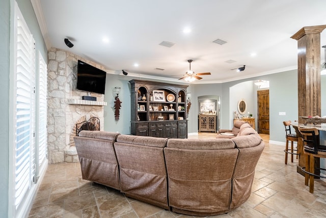 living room featuring ornamental molding, stone tile floors, visible vents, and a stone fireplace