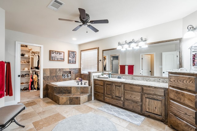bathroom with a bath, vanity, stone tile floors, visible vents, and a ceiling fan