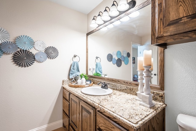 bathroom with baseboards, toilet, a textured wall, and vanity