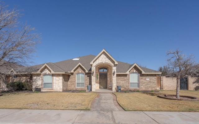 ranch-style house featuring brick siding, fence, a front yard, and stone siding