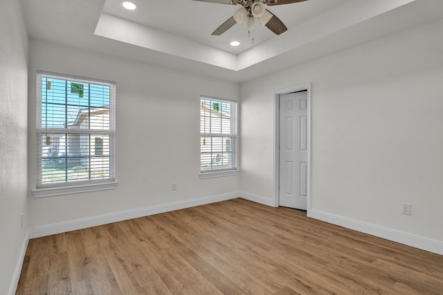 spare room featuring light wood finished floors, baseboards, ceiling fan, a tray ceiling, and recessed lighting