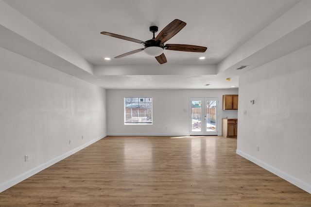 unfurnished living room with a tray ceiling, light wood-type flooring, visible vents, and baseboards