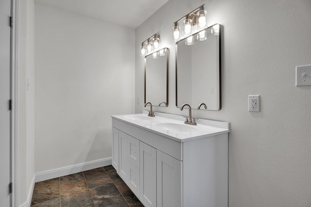 bathroom featuring stone finish flooring, double vanity, a sink, and baseboards