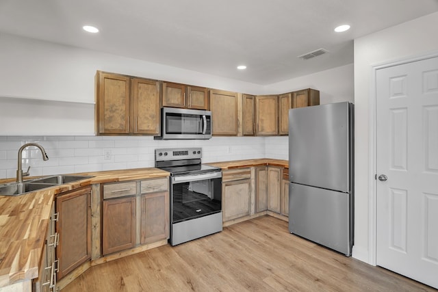 kitchen with light wood-type flooring, butcher block counters, appliances with stainless steel finishes, and a sink