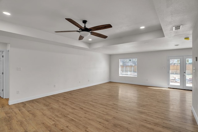 empty room featuring a tray ceiling, baseboards, and light wood finished floors