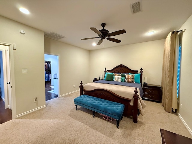 bedroom featuring a walk in closet, light colored carpet, a closet, and ceiling fan