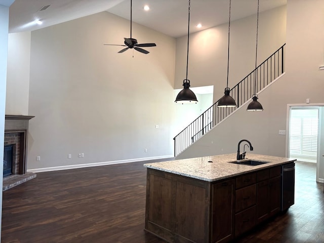 kitchen with ceiling fan, sink, pendant lighting, a fireplace, and an island with sink