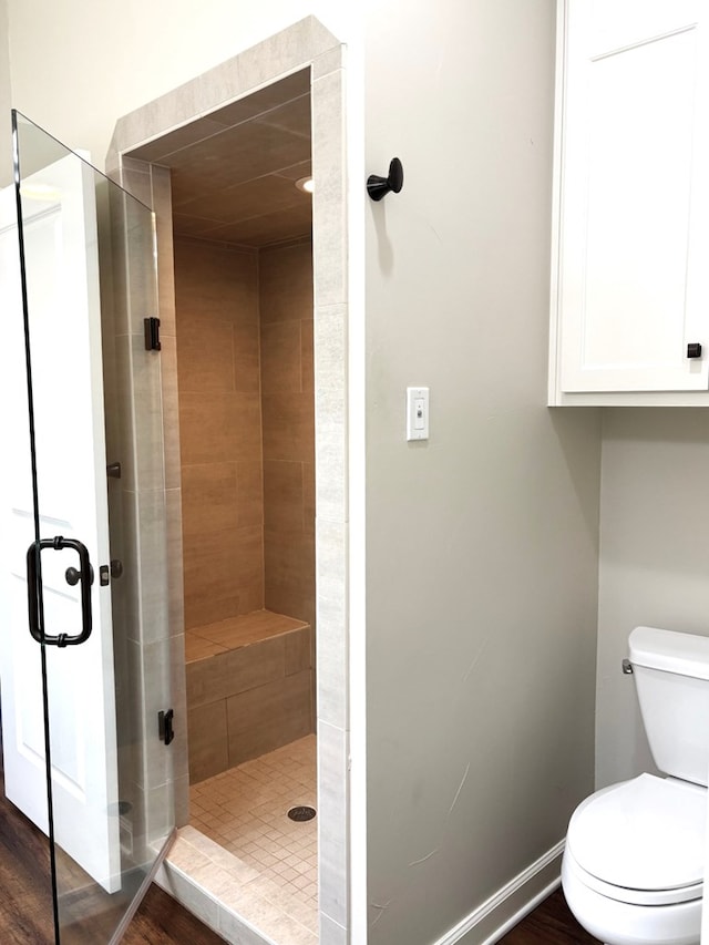 bathroom with hardwood / wood-style floors, toilet, and a shower with door